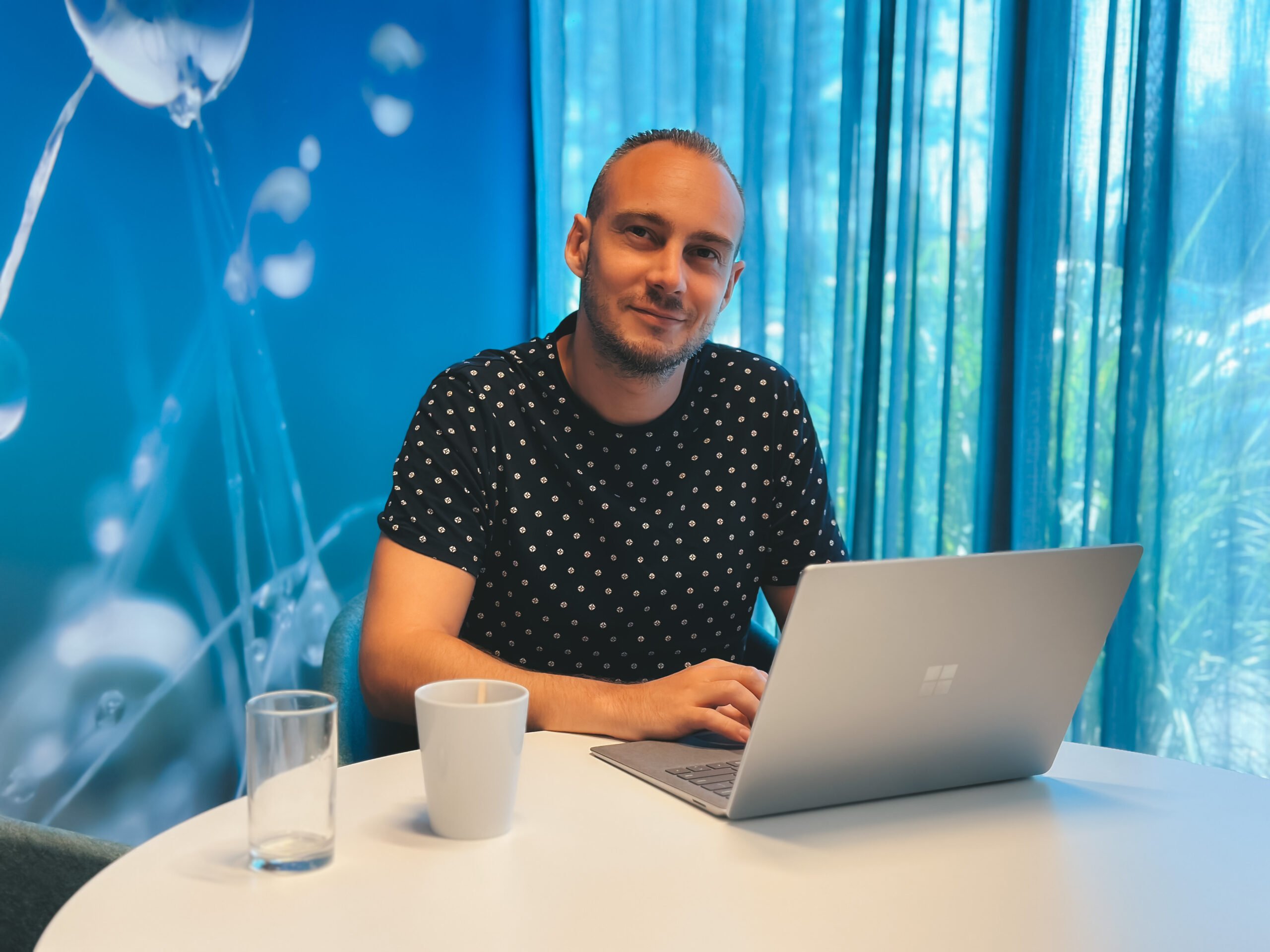 Roy op kantoor achter zijn laptop tegen een blauwe achtergrond - One way digital